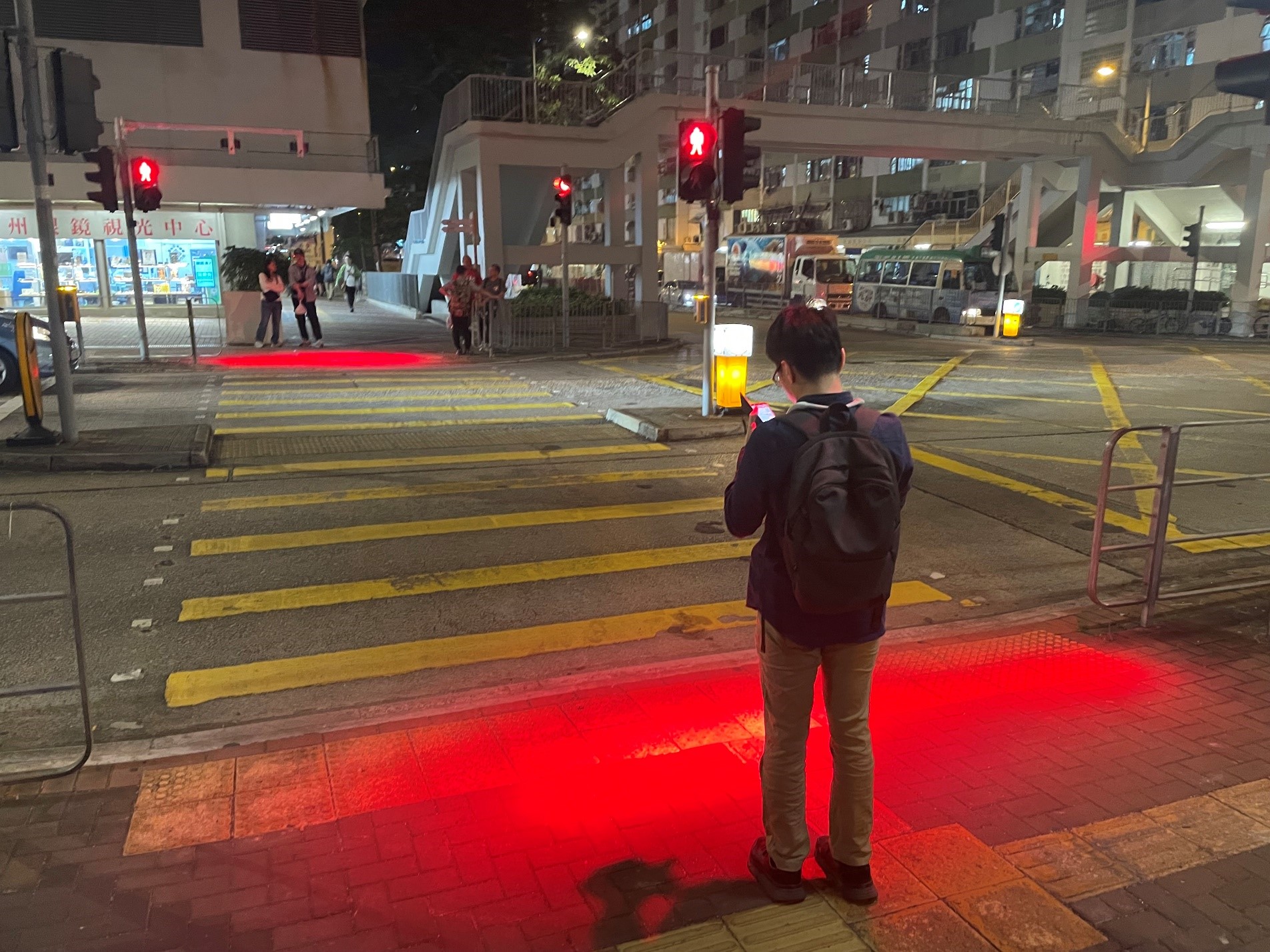 Pedestrian focus on smartphone with red light cast at night